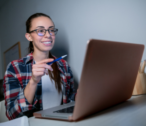 Schülerin sitzt am Laptop und lächelt während ihres Homeschoolunterrichts