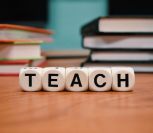 Würfel auf einem Lehrerpult, die das Wort Teach bilden