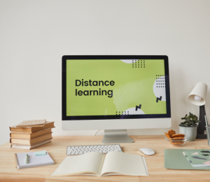 PC-Bildschirm mit Hintergrundschriftzug Distance Learning vor dem eine Tastatur und ein offenes Buch liegt